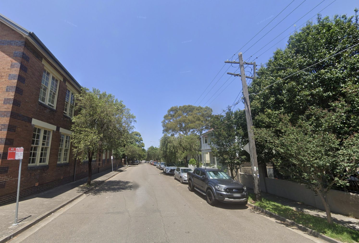 Cavendish Street looking down the hill: red-brick school building on the left, houses and a ute on the right.