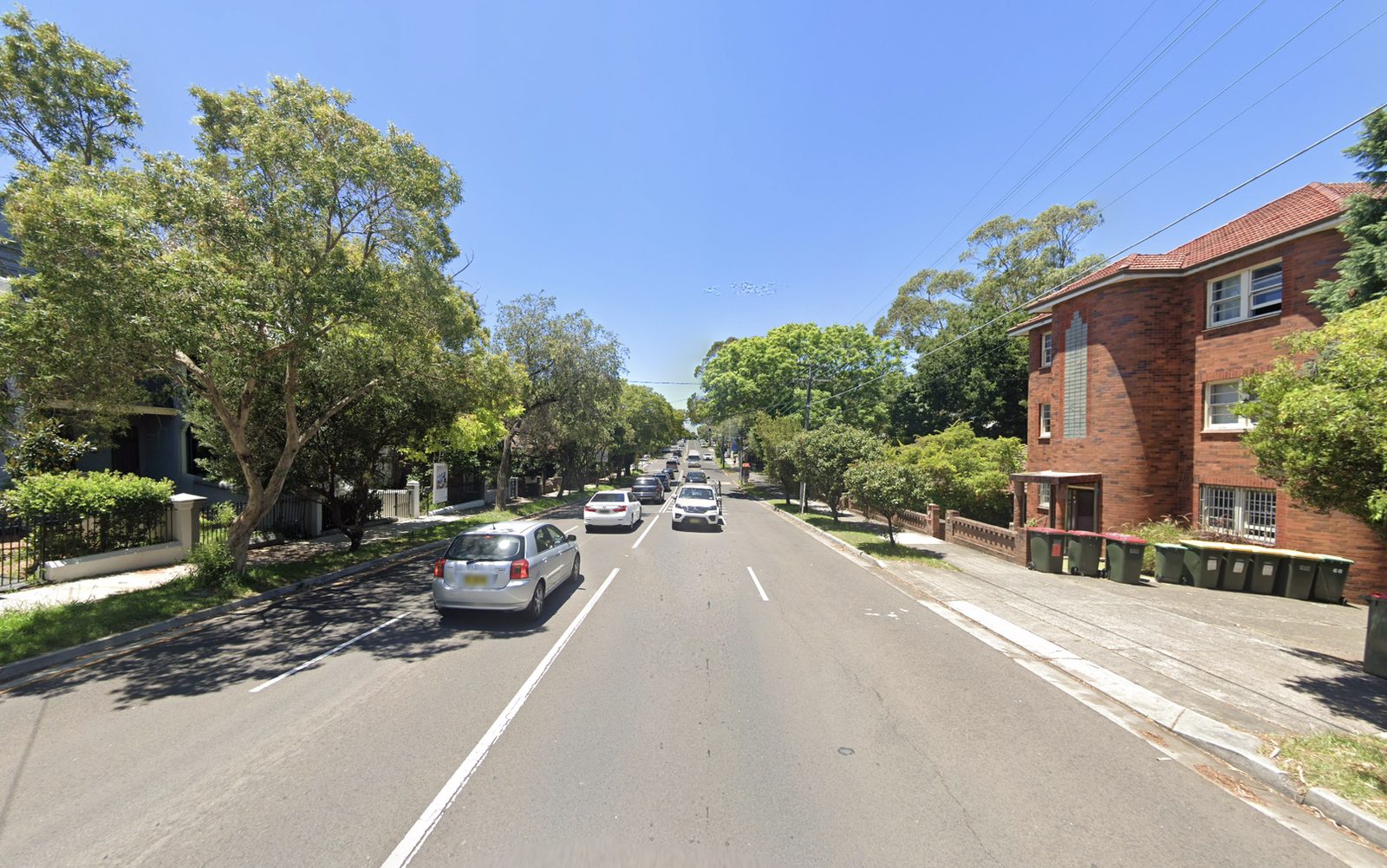 Stanmore Road looking up the hill: traffic, houses and trees on the left, red-brick flats on the right.